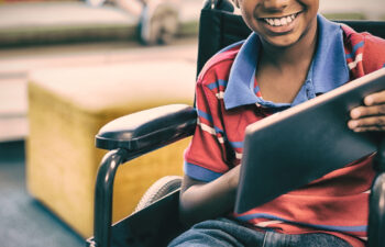 Portrait of disabled schoolboy on wheelchair using digital tablet in library at school