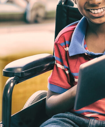 Portrait of disabled schoolboy on wheelchair using digital tablet in library at school
