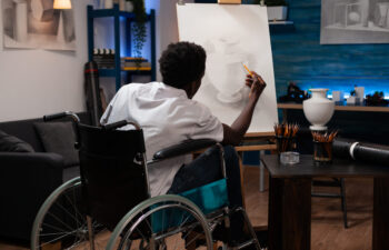 Young african american male artist user of wheelchair having good time making pencil drawing on canvas easel of pot. Man with artistic skills creating artwork at home art studio.