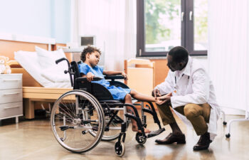 side view of african american doctor examining foot of disabled patient in wheelchair in clinic