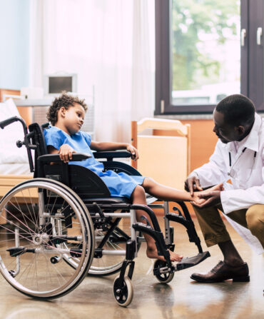 side view of african american doctor examining foot of disabled patient in wheelchair in clinic